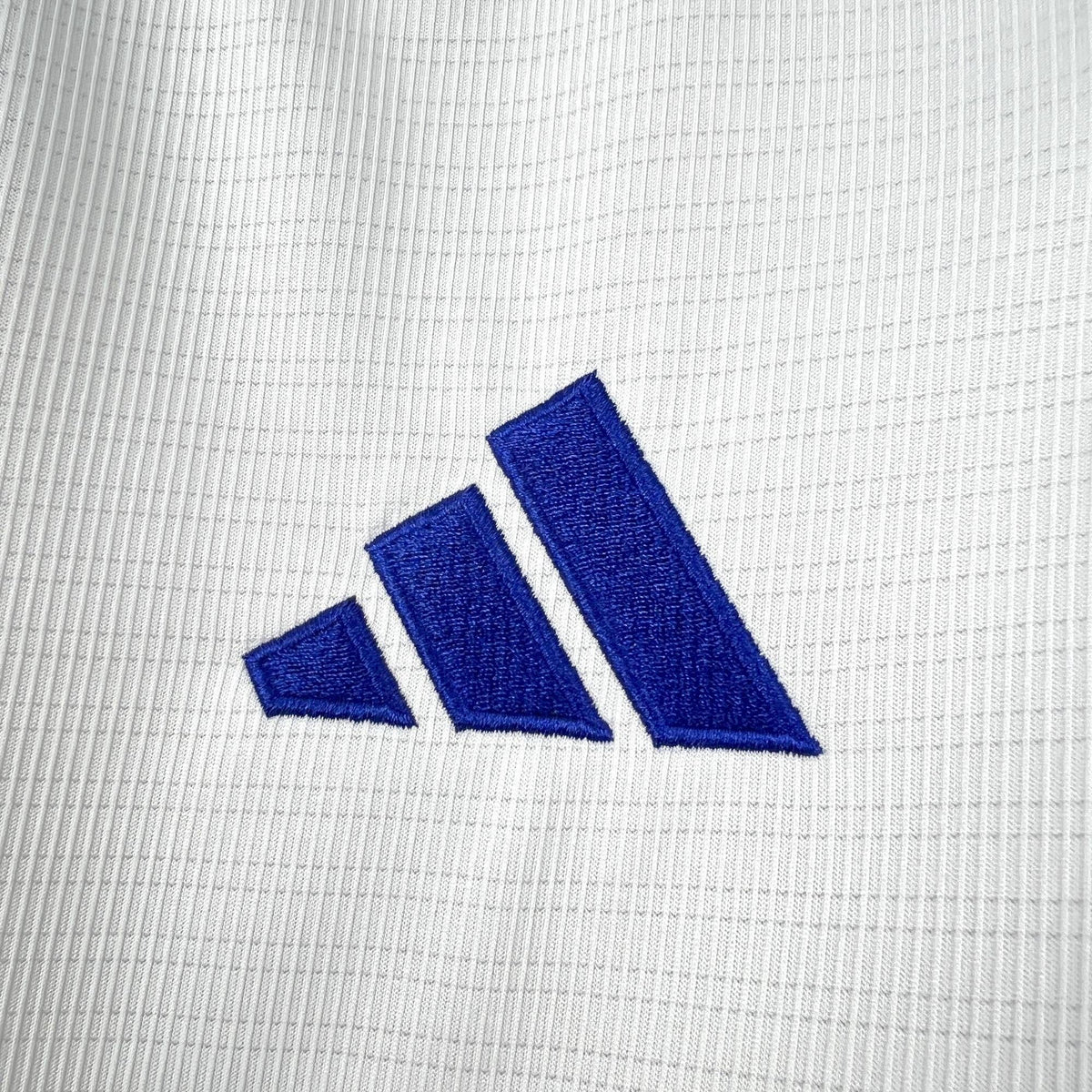 Close-up of the blue three-stripe chest mark on the white Greece Away Jersey 2026