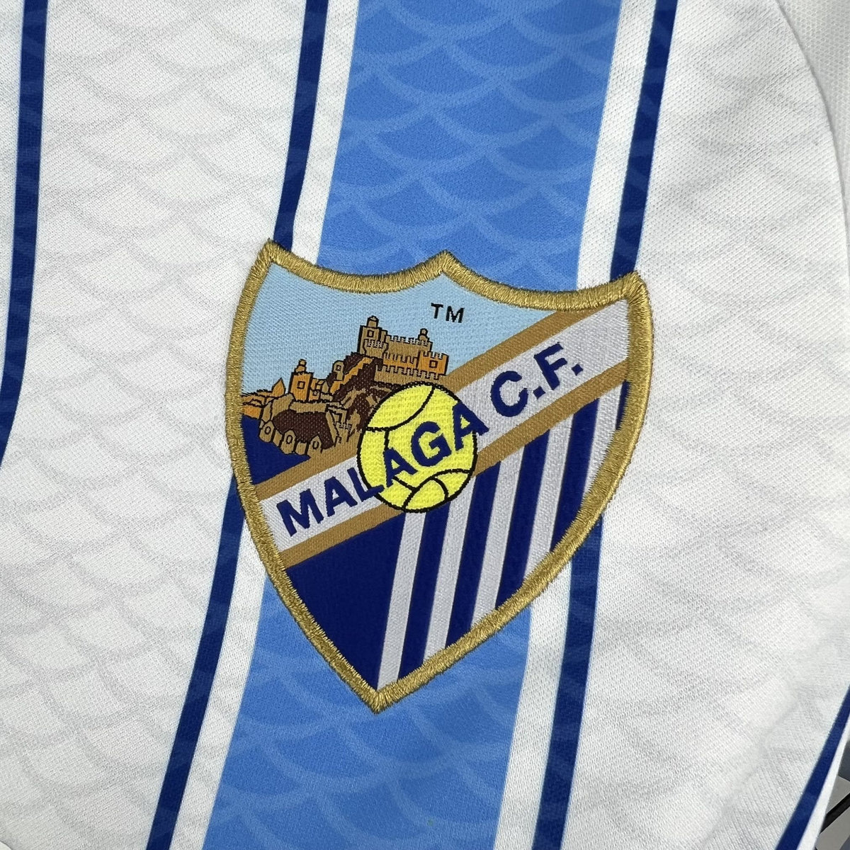 Close-up of the light blue stripe and fabric detail on the Málaga 2026/27 home jersey