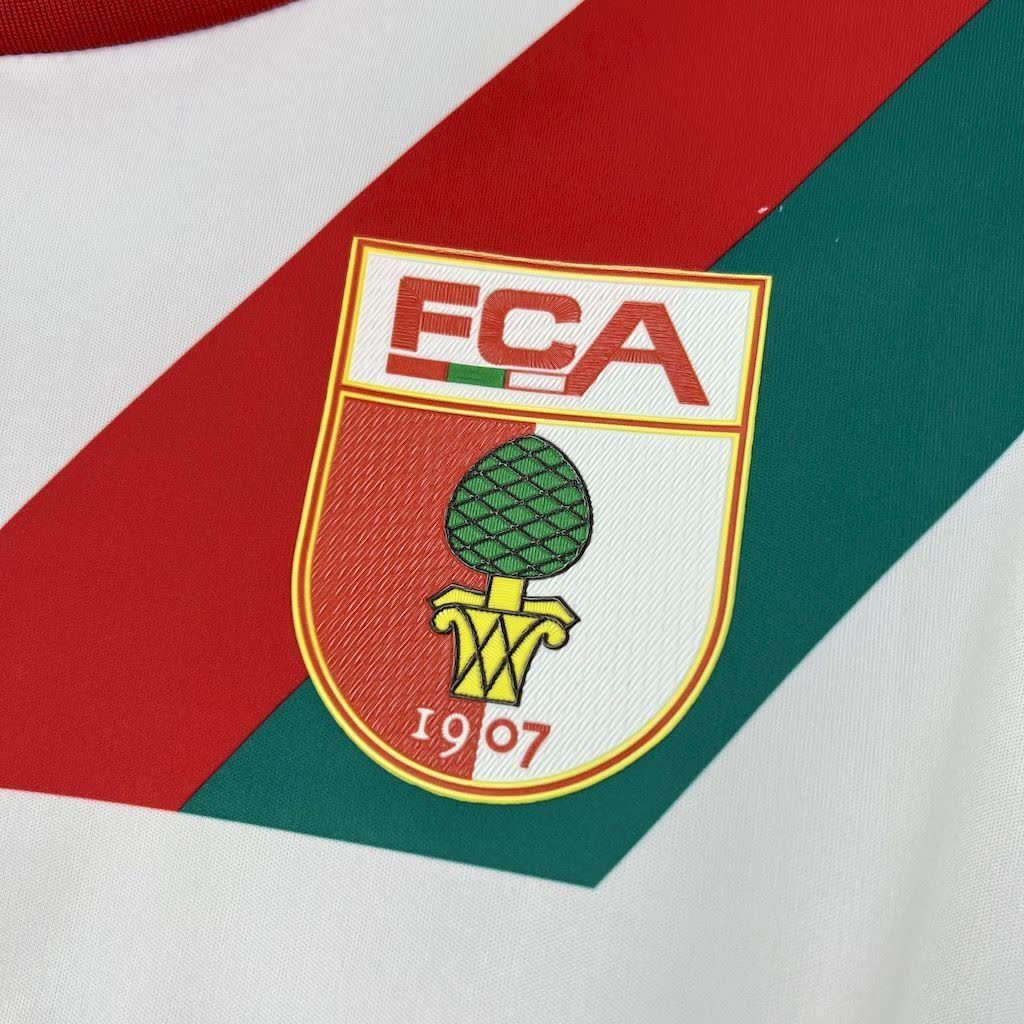 Close-up of the red chest logo and fabric on the FC Augsburg 2025/26 home jersey