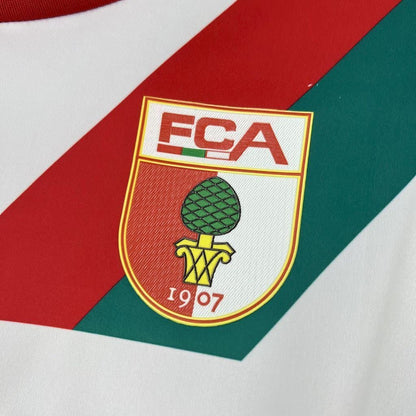 Close-up of the red chest logo and fabric on the FC Augsburg 2025/26 home jersey